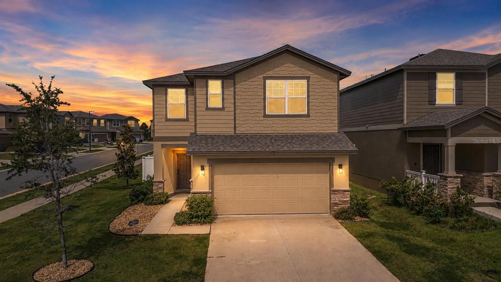 A two-story suburban house with tan siding, a two-car garage, and a concrete driveway — 2207 BEAR PEAK ROAD, MINNEOLA, FL