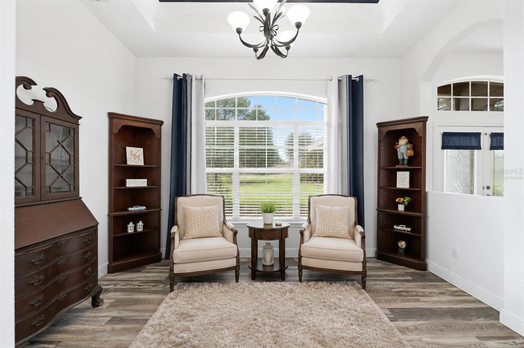 A bright sitting room features two armchairs, a small table, bookshelves, and a large window — 12041 SAPPHIRE DRIVE, SPRING HILL, FL