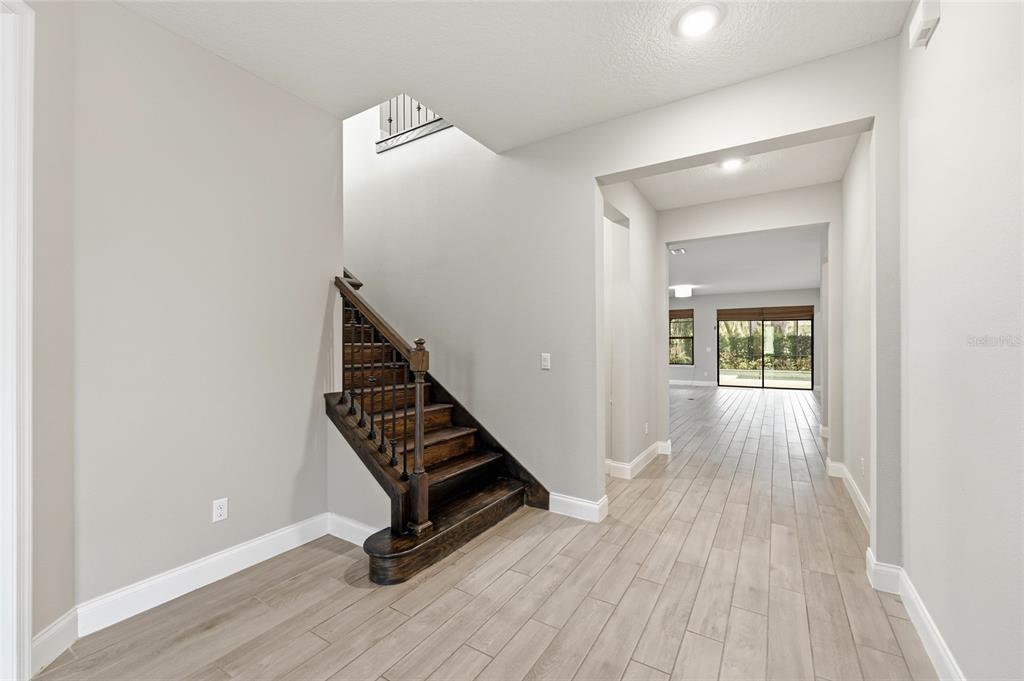 A foyer features light wood-look tile flooring, a dark wood staircase, and a hallway view — 8236 PROCIDA ISLE LANE, WINDERMERE, FL