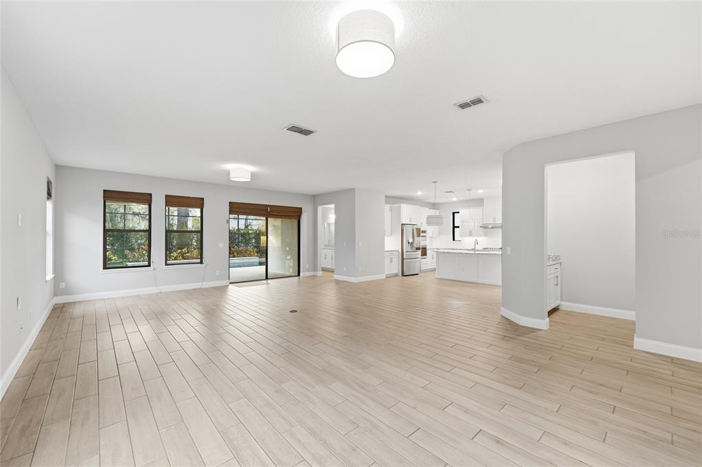 A bright, open-concept living area features light wood-look tile flooring and a view into the kitchen — 8236 PROCIDA ISLE LANE, WINDERMERE, FL