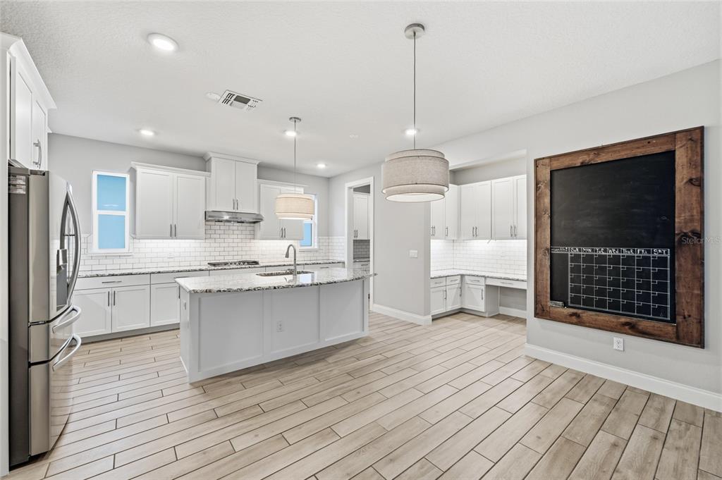 A modern kitchen features white cabinetry, a granite-topped island, stainless steel appliances, and wood-look flooring — 8236 PROCIDA ISLE LANE, WINDERMERE, FL
