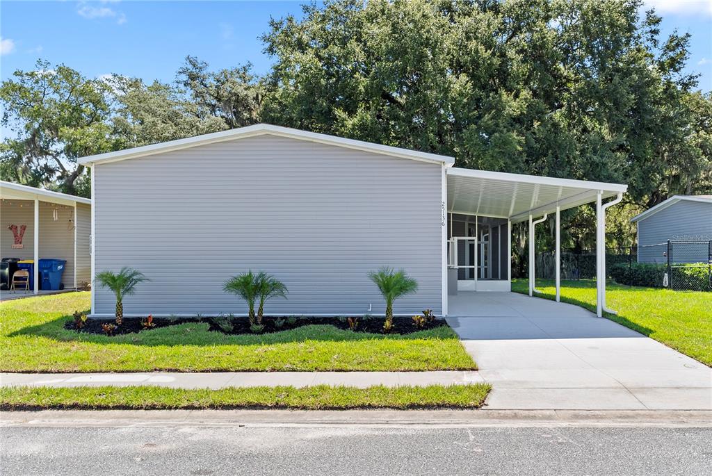 A gray single-story house with a carport and a small landscaped front yard — 25136 HUCKLEBERRY WAY, ASTATULA, FL