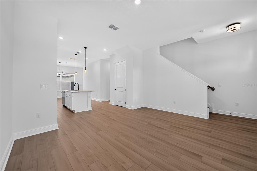 An open-concept living area features light wood-look flooring, white walls, and a kitchen island — 13321 LUSH LIME ALLEY, WINDERMERE, FL