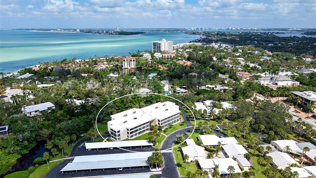 An aerial view shows a multi-story white apartment building surrounded by lush greenery and parking — 225 HOURGLASS WAY UNIT 106, SARASOTA, FL