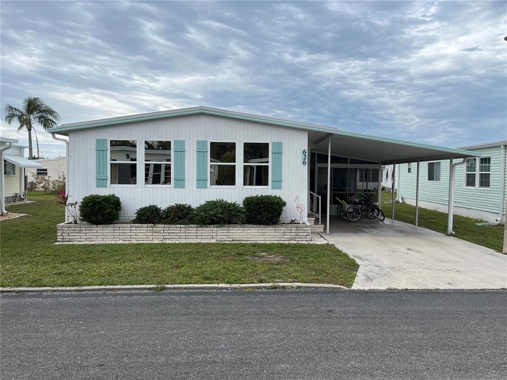 A single-story manufactured home with light siding, blue shutters, and an attached carport — 626 CERVINA DRIVE, VENICE, FL