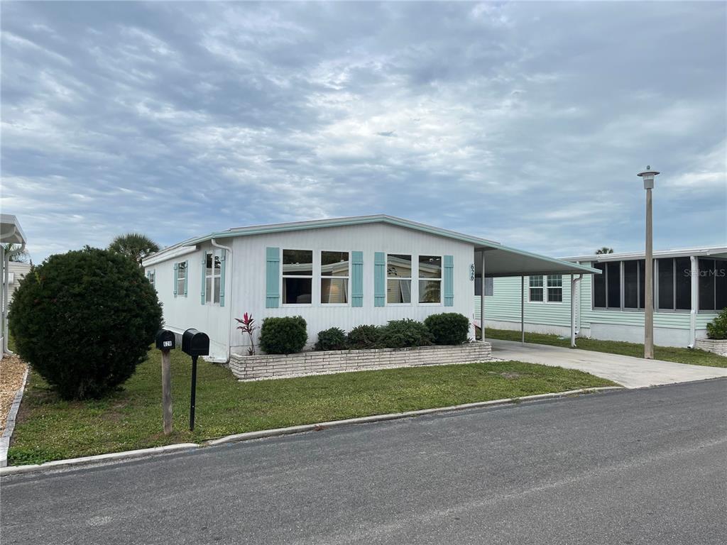 A single-story mobile home with white siding, blue shutters, and an attached carport — 626 CERVINA DRIVE, VENICE, FL