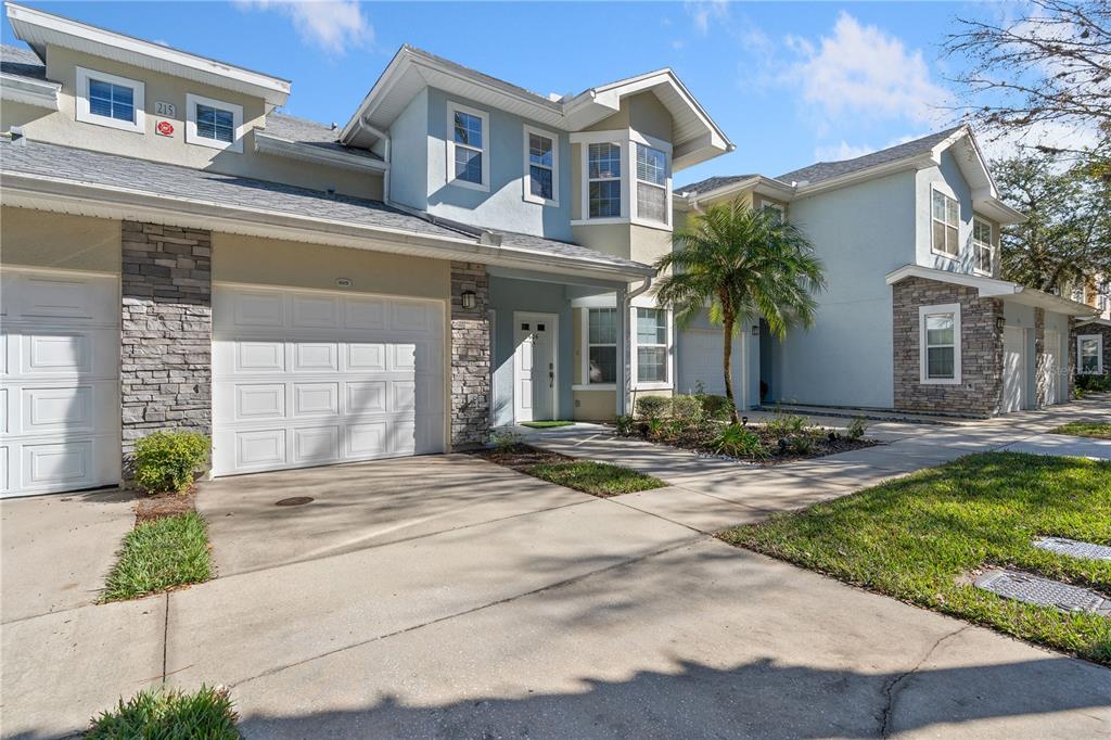 A two-story townhouse exterior features a white garage, stone accents, and a paved driveway — 215 BAYBERRY CIRCLE UNIT 605, ST AUGUSTINE, FL