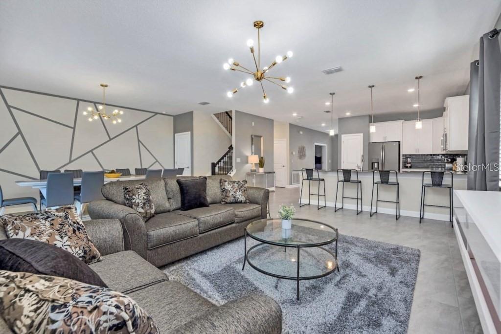An open-concept living room and kitchen featuring gray tile floors, a geometric accent wall, and chandeliers — 2846 BOOKMARK DRIVE, KISSIMMEE, FL
