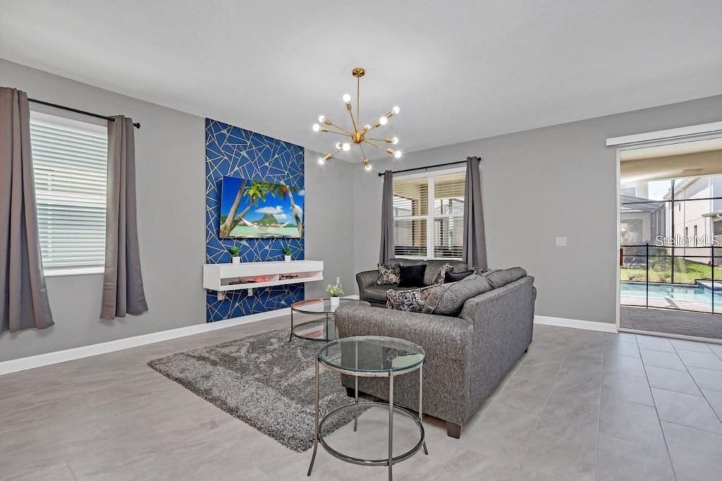 A living room features a blue geometric accent wall, gray sofa, and a glass chandelier — 2846 BOOKMARK DRIVE, KISSIMMEE, FL
