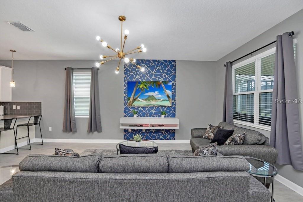 A living room features a gray sofa, a geometric accent wall, and a modern chandelier — 2846 BOOKMARK DRIVE, KISSIMMEE, FL