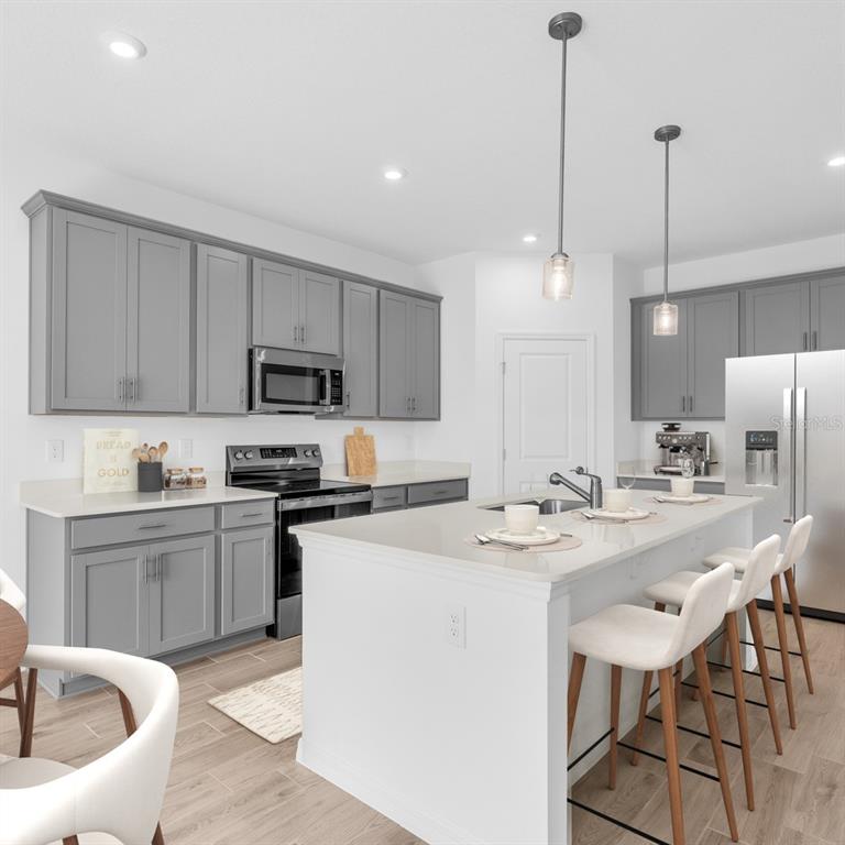 A kitchen features grey cabinets, white countertops, a central island with seating, and stainless appliances — 9237 HARRIS HAWK DRIVE, LEESBURG, FL