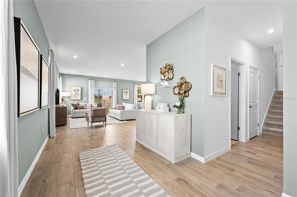 A bright, open-concept living area features light-colored walls, wood-look tile flooring, and a staircase — 4421 RIVER BEACON BOULEVARD, DAVENPORT, FL