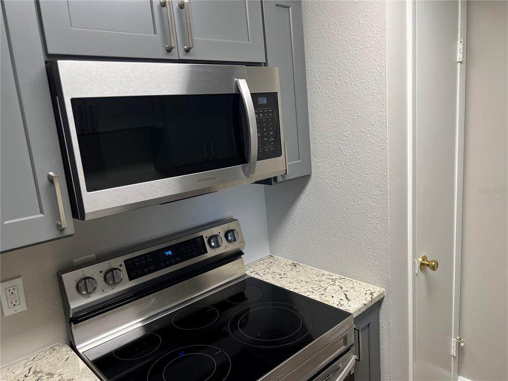 A kitchen features gray cabinets, a stainless steel microwave, and a black electric range — 208 RED CEDAR PLACE UNIT 208, BRANDON, FL