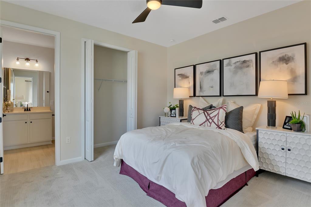 A bedroom features a bed with a purple skirt, wall art, and an attached bathroom — 164 FLAG LILLY LANE, UMATILLA, FL