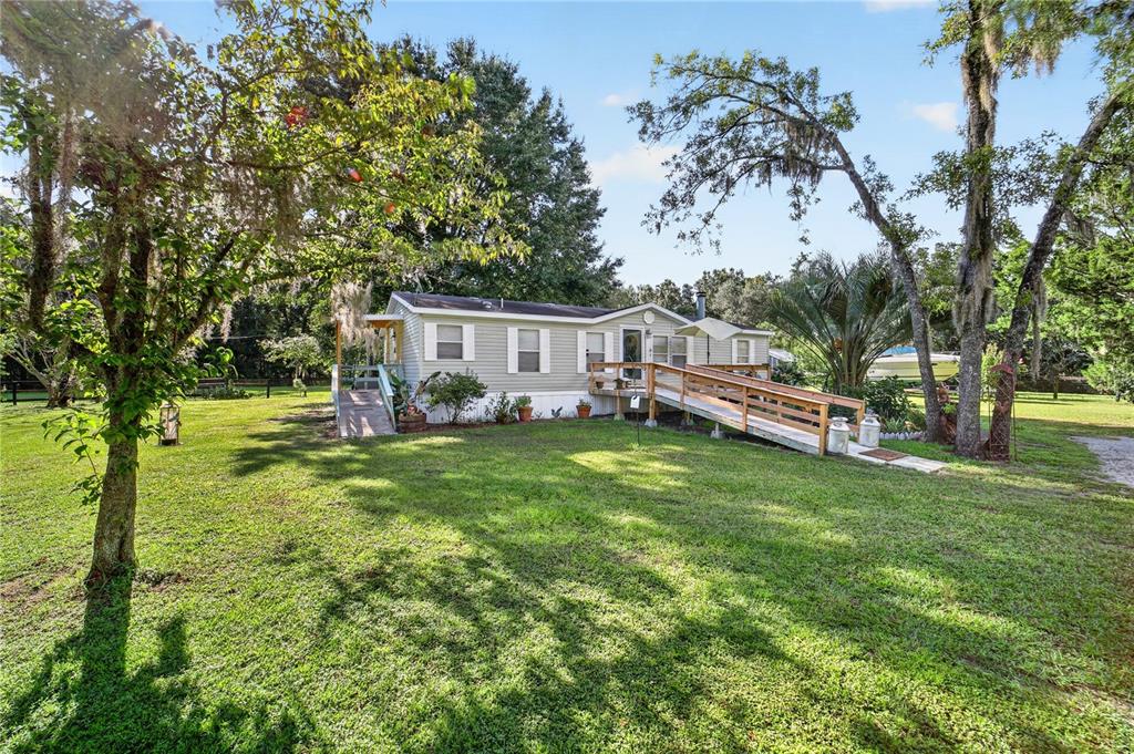 A light-colored manufactured home features a wooden wheelchair ramp leading to the front entrance — 6051 SE 148TH TERRACE, MORRISTON, FL