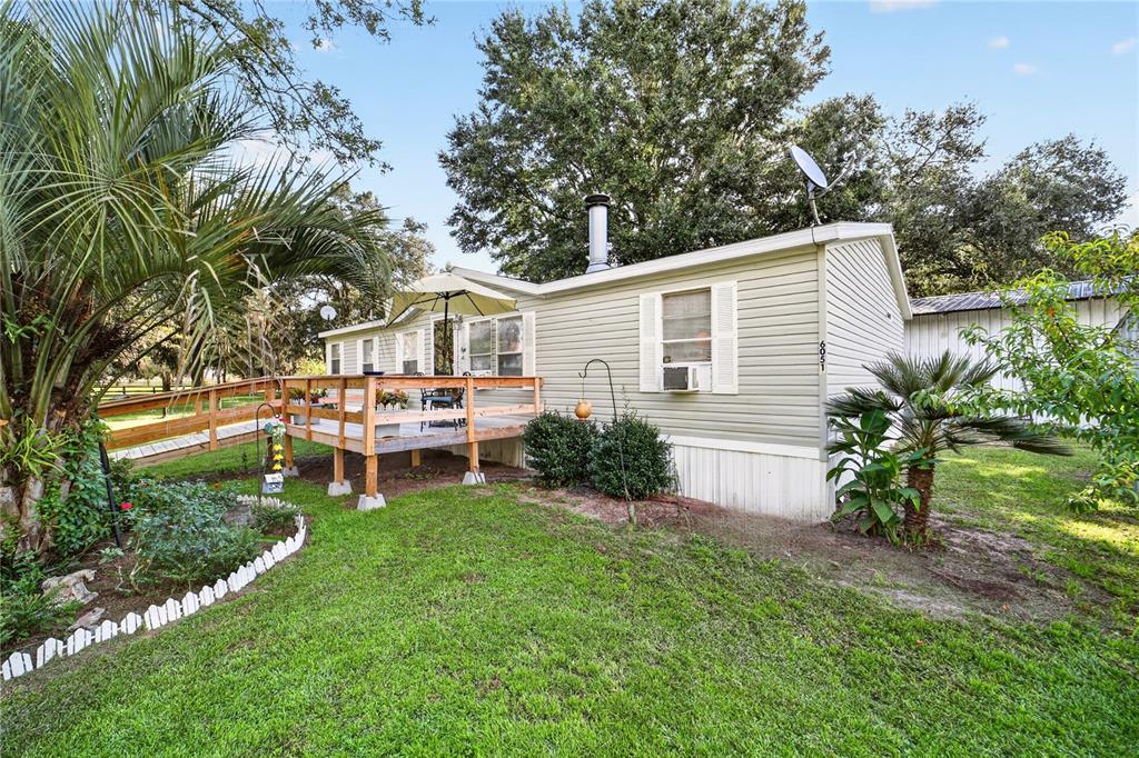 A light green mobile home features a wooden deck with a ramp and palm trees — 6051 SE 148TH TERRACE, MORRISTON, FL