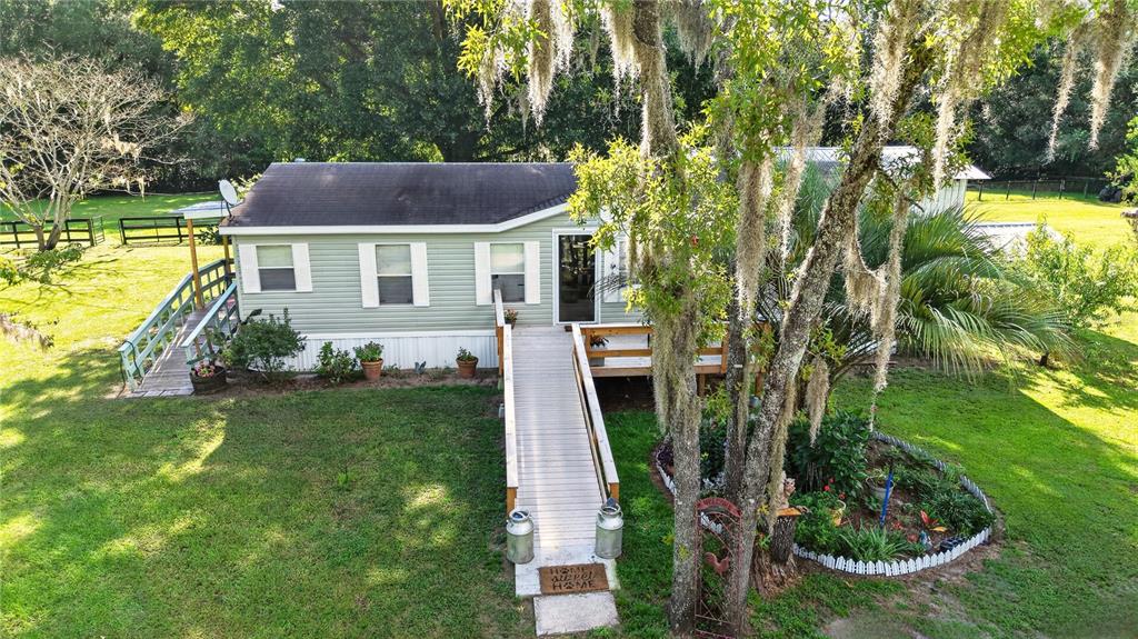 An exterior view of a light green manufactured home with a wooden ramp and deck — 6051 SE 148TH TERRACE, MORRISTON, FL