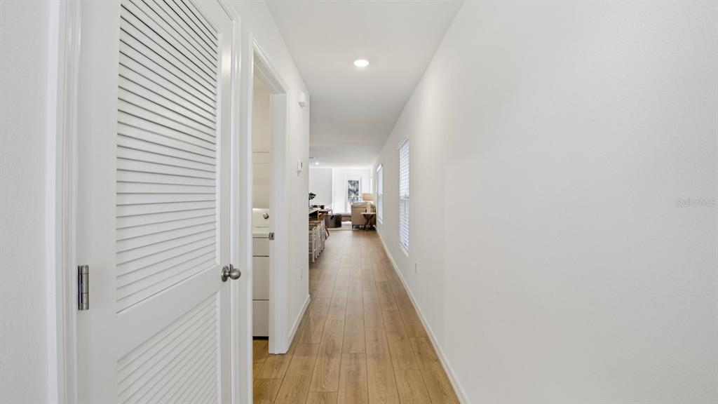 A hallway with light wood-look flooring leads toward a living area with a laundry closet — 17841 MOUNT BLACKBURN LANE, SPRING HILL, FL