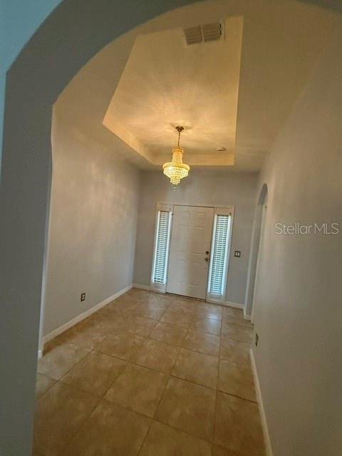 An entryway with a tray ceiling, a crystal chandelier, and light-colored tile flooring — 3817 MT VERNON WAY, KISSIMMEE, FL