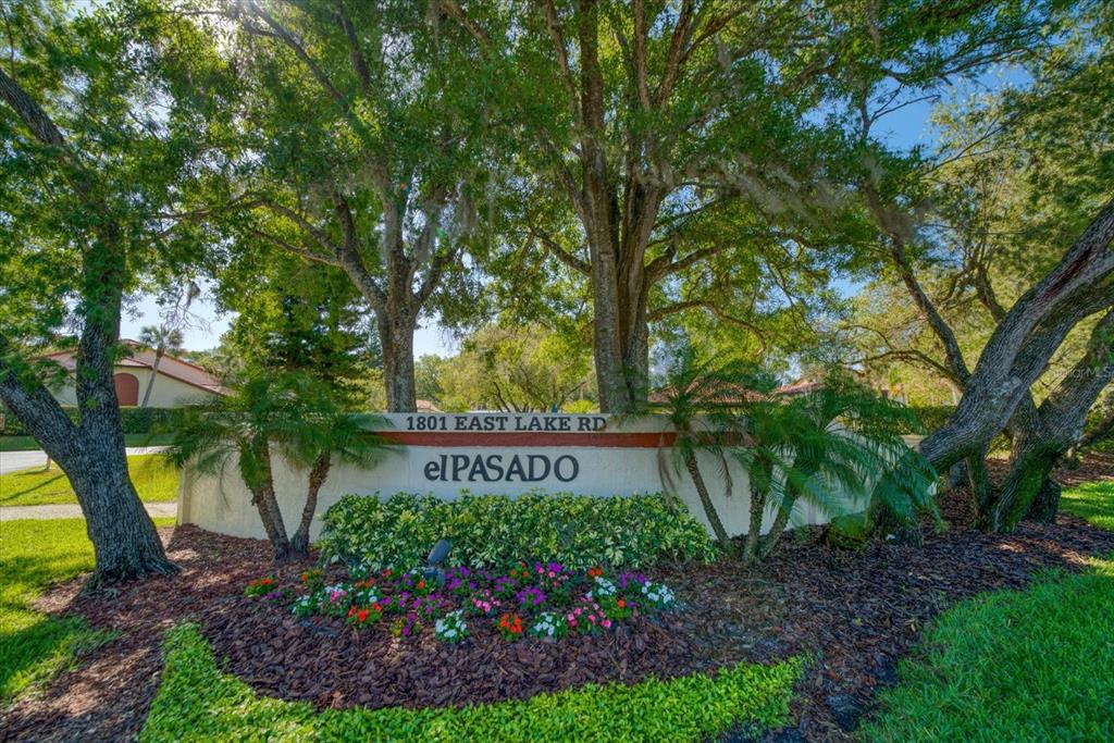 A stone monument sign for the El Pasado community sits beneath large, moss-draped oak trees — 1801 E LAKE ROAD UNIT 10D, PALM HARBOR, FL