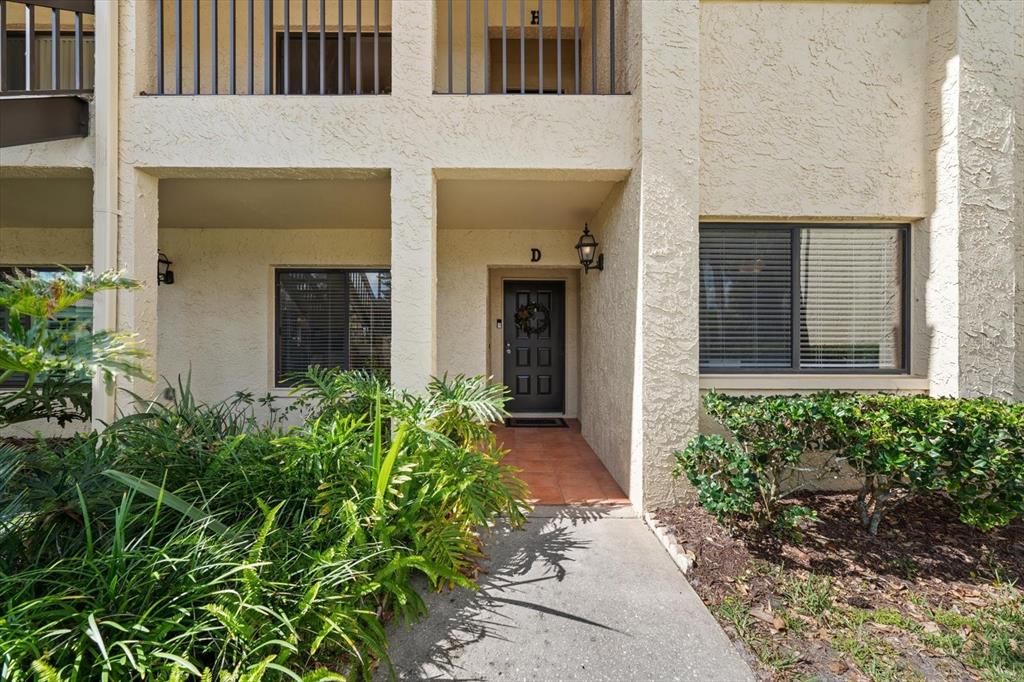 The exterior of a multi-story apartment building features a ground-level entrance with a dark door — 1801 E LAKE ROAD UNIT 10D, PALM HARBOR, FL