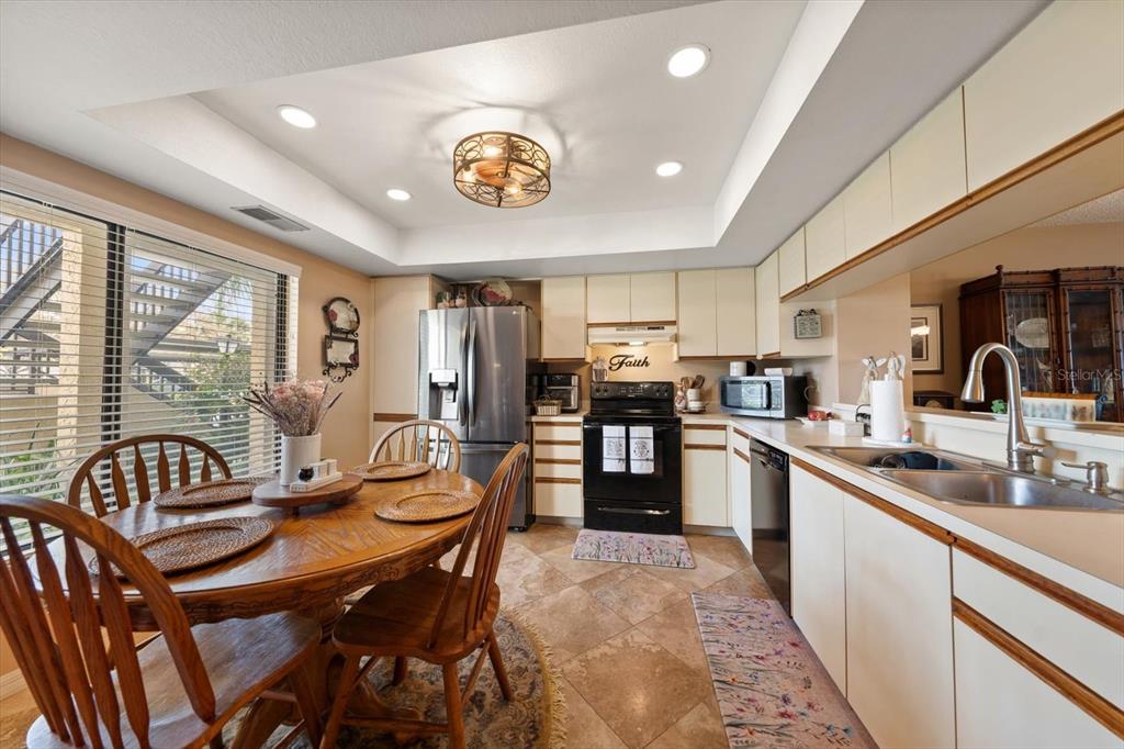 A kitchen with light cabinets, black appliances, a dining table, and tile flooring — 1801 E LAKE ROAD UNIT 10D, PALM HARBOR, FL
