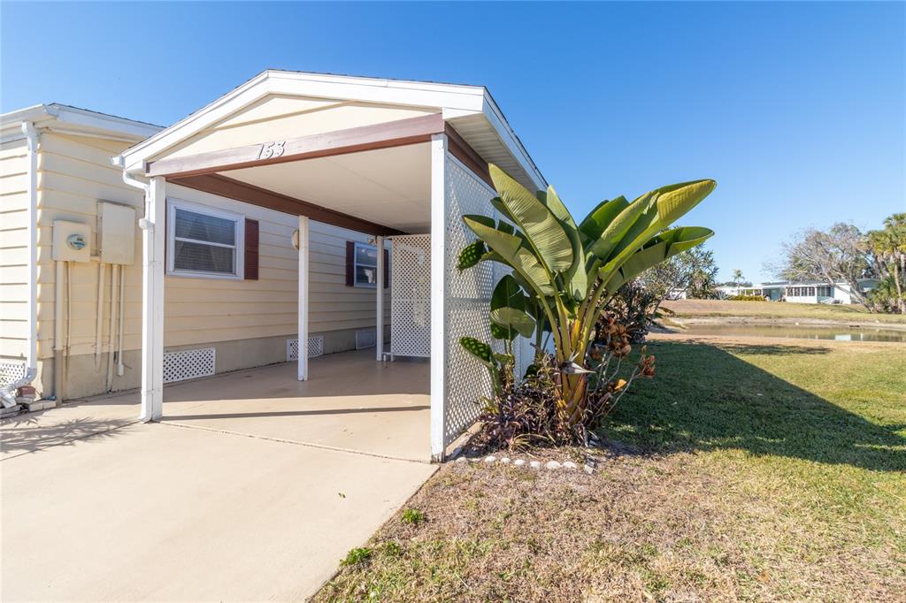 A mobile home exterior features a covered carport with white lattice siding and a large plant — 153 EGRET CIRCLE, ELLENTON, FL