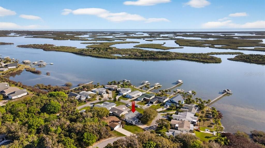 An aerial view shows a waterfront neighborhood with a red arrow pointing to a house — 332 MARSH LANDING LOOP, OAK HILL, FL