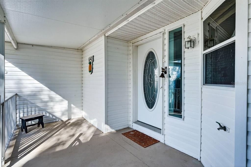 A covered front porch features white horizontal siding, a glass-paneled door, and a small bench — 332 MARSH LANDING LOOP, OAK HILL, FL