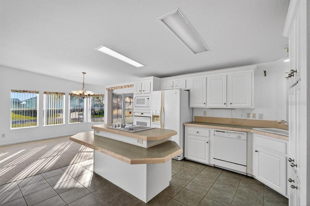 A kitchen with white cabinets, tile countertops, a central island, and an adjacent dining area — 332 MARSH LANDING LOOP, OAK HILL, FL