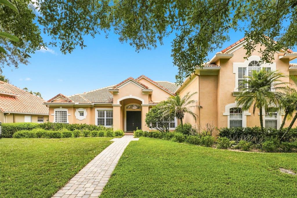 A tan stucco house with a tiled roof, arched entryway, and a brick walkway — 7746 DEBEAUBIEN DRIVE, ORLANDO, FL