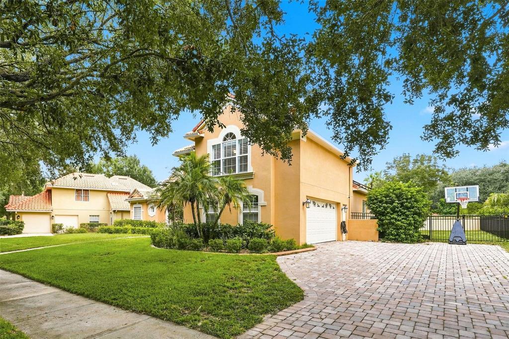 A two-story stucco house with a paved driveway, a basketball hoop, and a grassy lawn — 7746 DEBEAUBIEN DRIVE, ORLANDO, FL