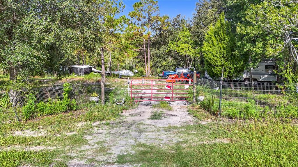 A red metal gate opens onto a dirt driveway leading to a wooded residential lot — 0 THOMAS BOULEVARD, HUDSON, FL