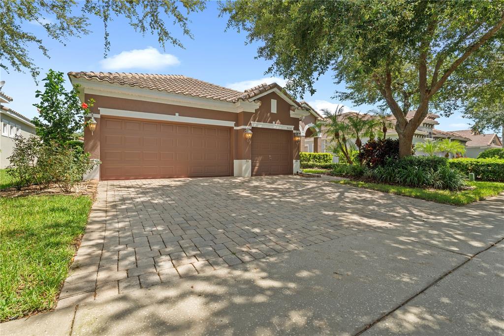 A brown single-story house with a three-car garage and a paved driveway under shade trees — 9018 VIA BELLA NOTTE, ORLANDO, FL