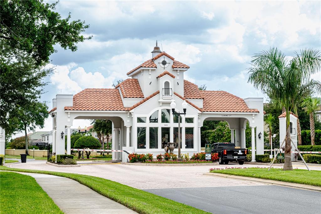 A gated community entrance features a stucco guardhouse with a tiled roof and palm trees — 9018 VIA BELLA NOTTE, ORLANDO, FL