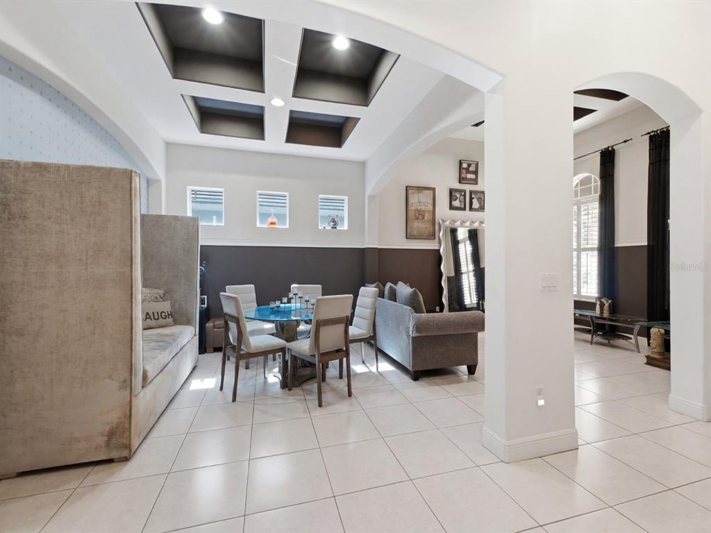 A dining area features a glass table, upholstered chairs, a high-backed bench, and coffered ceilings — 9018 VIA BELLA NOTTE, ORLANDO, FL