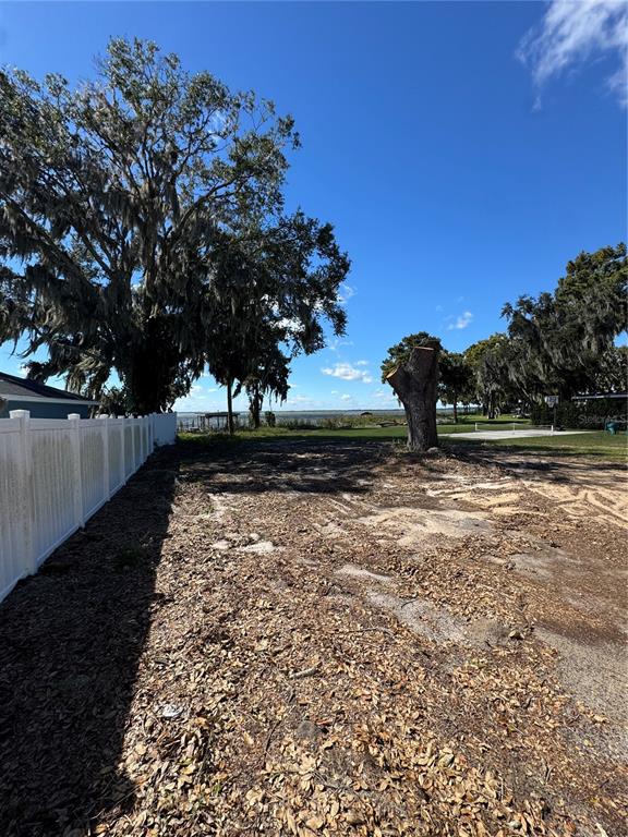 A vacant, leaf-covered lot features a large tree stump and a white vinyl fence — 1200 NORTHSHORE DRIVE, EUSTIS, FL