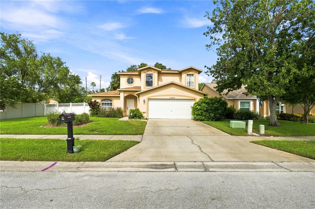 A two-story suburban house with a beige stucco exterior, a two-car garage, and a lawn — 1220 ALEXANDER WAY, LARGO, FL