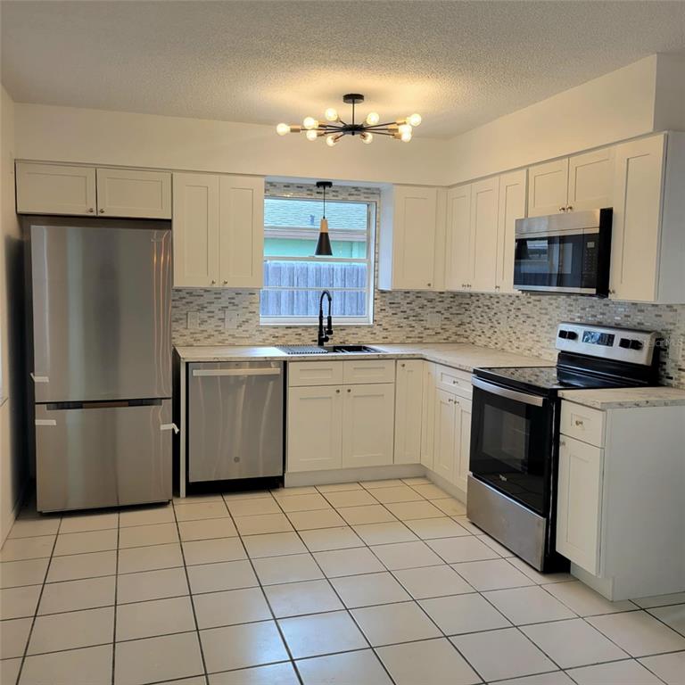 A kitchen features white cabinets, stainless steel appliances, a tiled backsplash, and a central light fixture — 8504 LAFITTE DRIVE, HUDSON, FL