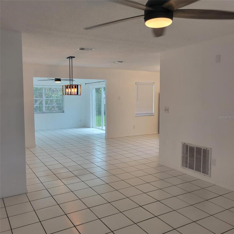 An open-concept room with white tile floors, a ceiling fan, and a hanging light fixture — 8504 LAFITTE DRIVE, HUDSON, FL