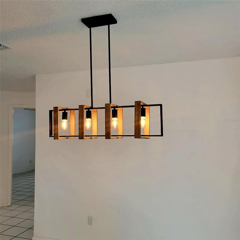 A modern rectangular chandelier with wood and black metal frames hangs in a white room — 8504 LAFITTE DRIVE, HUDSON, FL