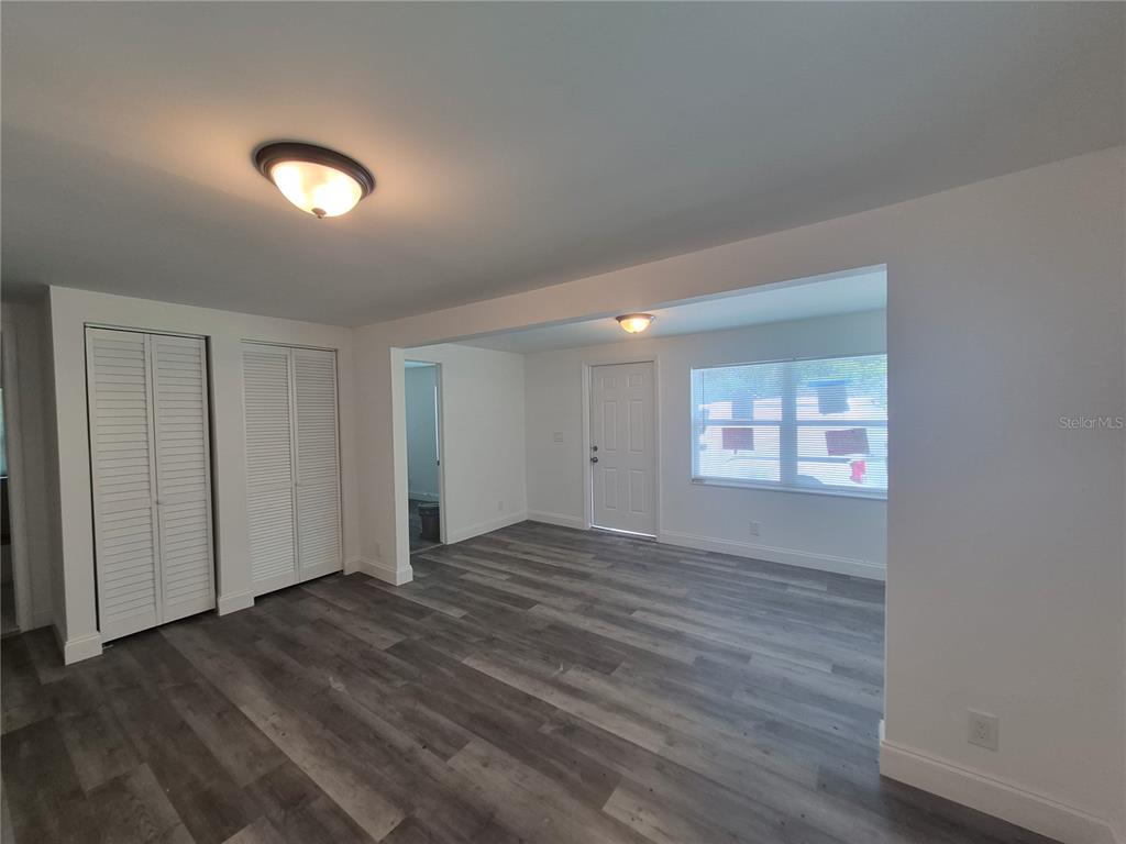A living room features white walls, gray wood-look flooring, louvered closet doors, and a front door — 12599 NW 38TH AVENUE, REDDICK, FL