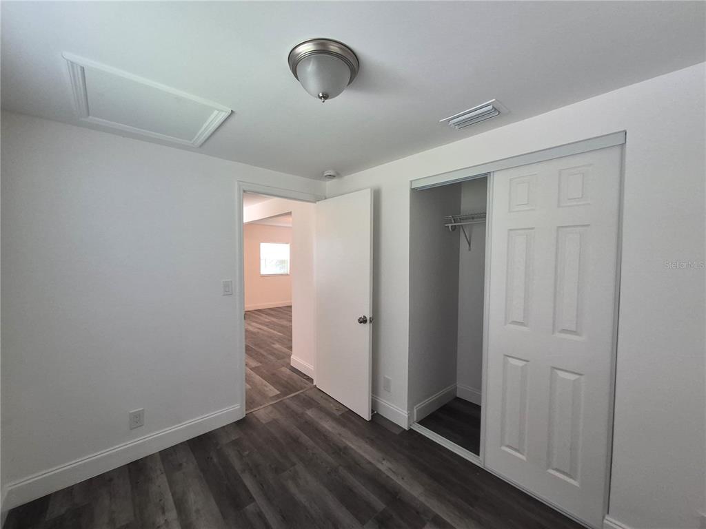 A bedroom features gray wood-look flooring, a white closet with sliding doors, and a doorway — 12599 NW 38TH AVENUE, REDDICK, FL