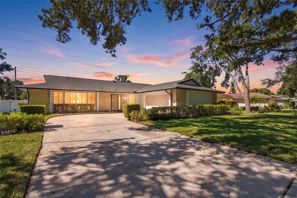 A single-story house with a concrete driveway and large trees at sunset — 2942 CLUBHOUSE DRIVE W, CLEARWATER, FL