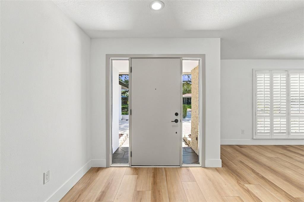 A bright entryway features light wood flooring, white walls, and a door with side windows — 2942 CLUBHOUSE DRIVE W, CLEARWATER, FL