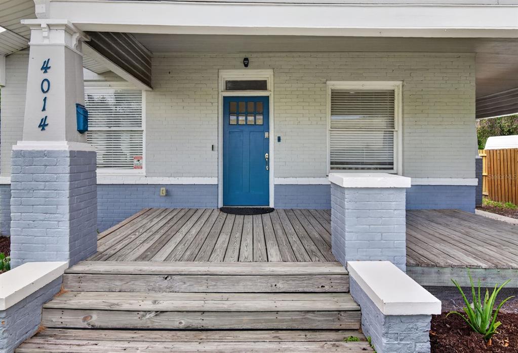 A front porch with wooden decking, brick columns, and a blue door on a house — 4014 N MARGUERITE STREET, TAMPA, FL