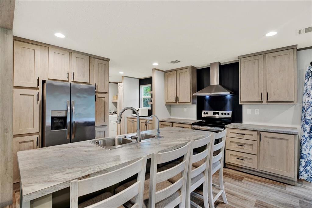 A kitchen features light wood cabinets, a stone-topped island with a sink, and stainless appliances — 2845 N LAKEFRONT DRIVE, HERNANDO, FL