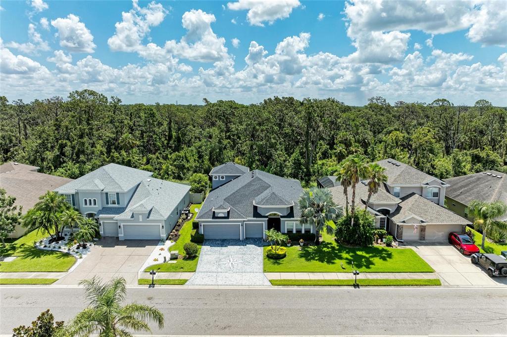 An aerial view shows three suburban houses with driveways and lawns bordering a dense forest — 7812 115TH AVENUE E, PARRISH, FL
