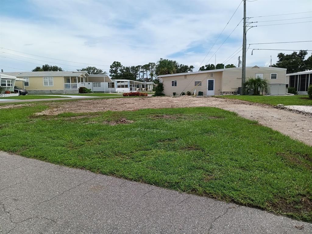 A vacant lot with grass and dirt sits between two mobile homes under a cloudy sky — 825 CAREFREE, VENICE, FL