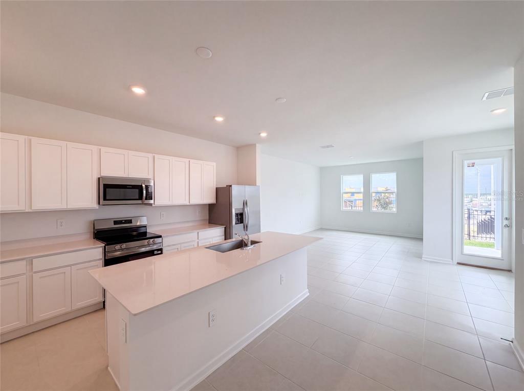 A modern kitchen features white cabinets, a quartz island, stainless steel appliances, and tile flooring — 3102 KURTZ TERRACE, DAVENPORT, FL